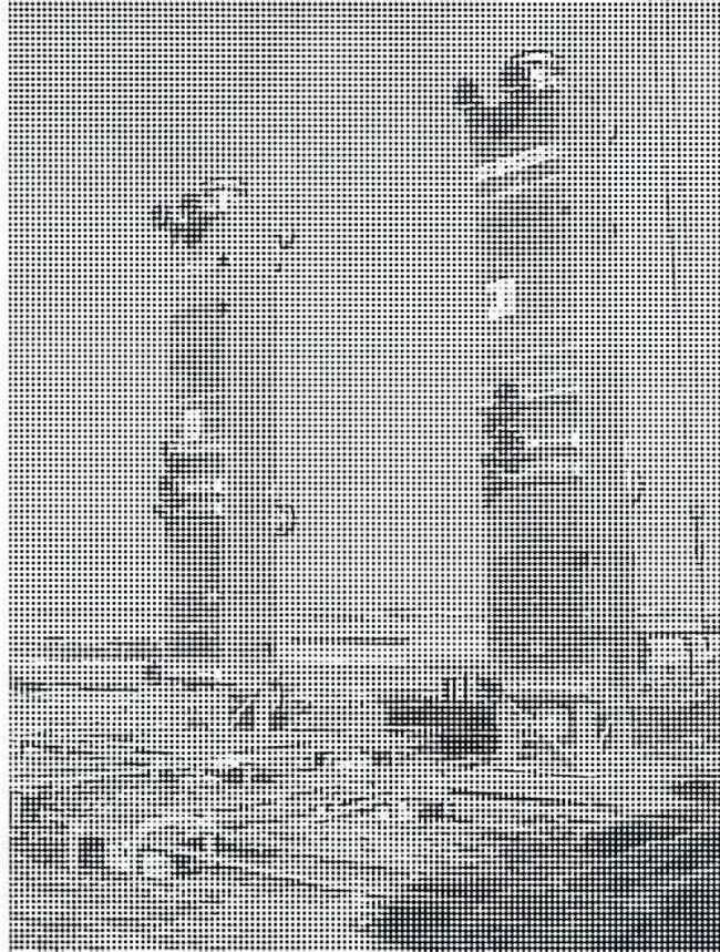 A black and white photograph showing a large, complex industrial heat exchanger unit. The unit consists of several vertical cylindrical tanks connected by a network of pipes and valves. It is situated outdoors on a flat, open landscape under a clear sky.