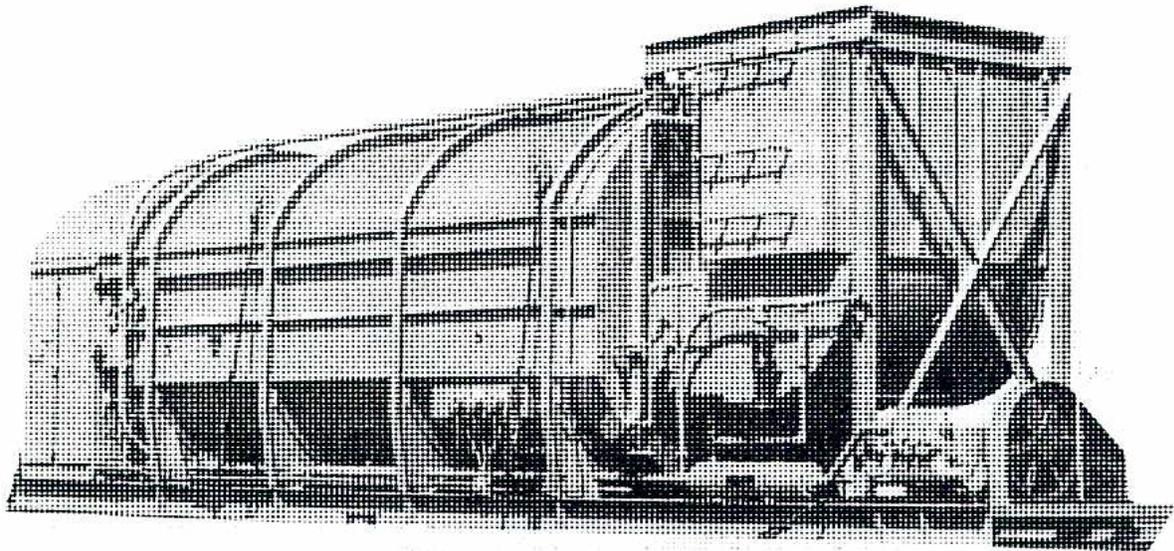 A black and white photograph of a large, horizontal, skid-mounted packaged steam-flood boiler. The boiler is a long, cylindrical tank with several horizontal bands or rings around its body. It is mounted on a metal frame with four legs. Various pipes, valves, and fittings are visible on top and around the boiler. The background is a plain, light-colored surface.
