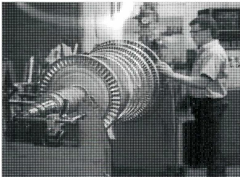 A black and white photograph showing a large turbine rotor assembly resting on a support structure. The rotor consists of a central shaft with multiple sets of blades (stator vanes) and a large, flanged disc. The assembly is positioned horizontally, and the background shows industrial equipment and structural elements.