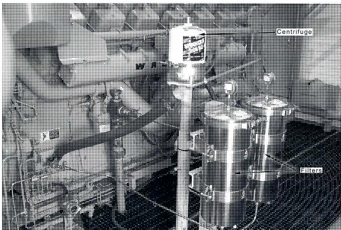 A black and white photograph of an engine's internal components, showing the oil filtration system. A label 'Centrifuge' points to a cylindrical component on the right side of the image. Another label 'Filters' points to a series of three stacked, bowl-shaped components below the centrifuge. Various pipes and engine parts are visible in the background.