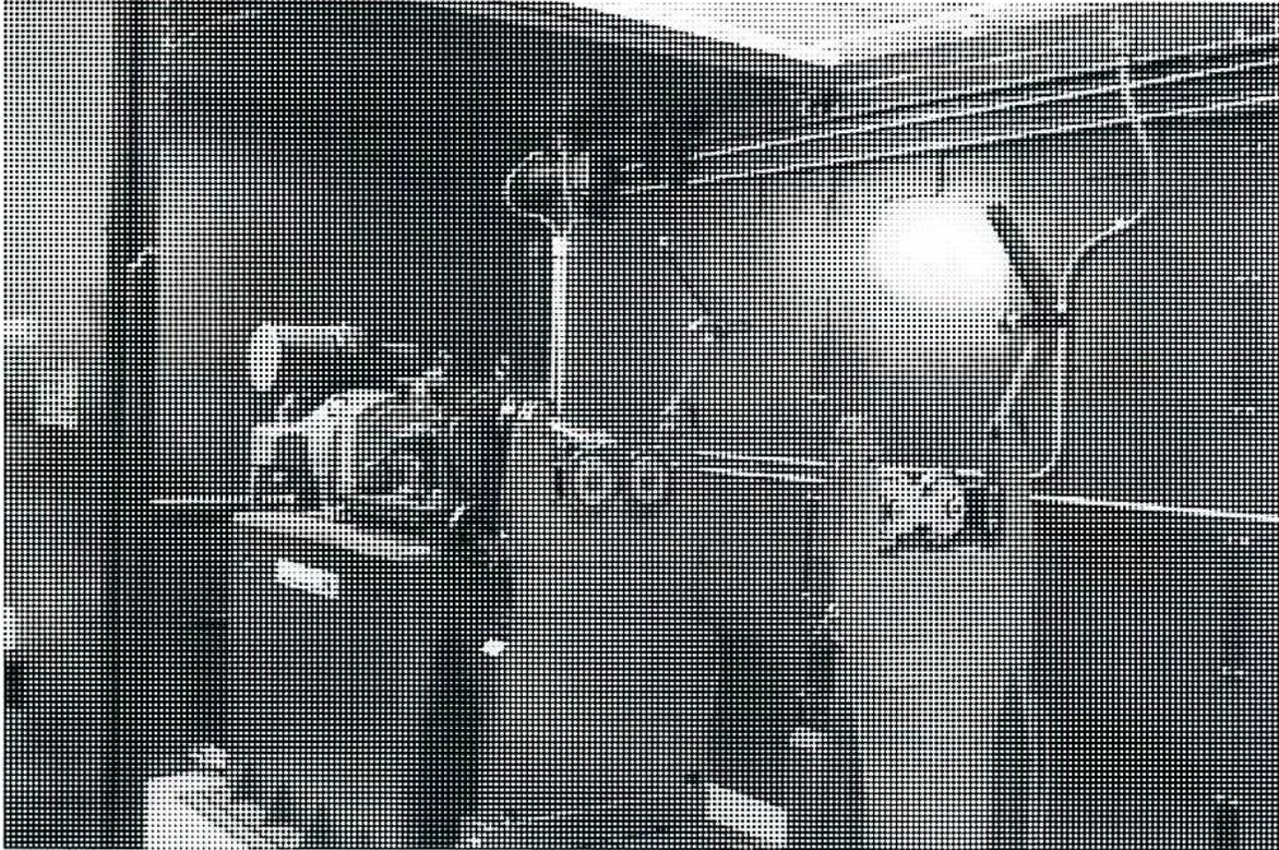 A black and white photograph of a rotor being balanced in a balancing machine. The rotor is mounted on a stand with various adjustment knobs and sensors. The background is dark and textured.