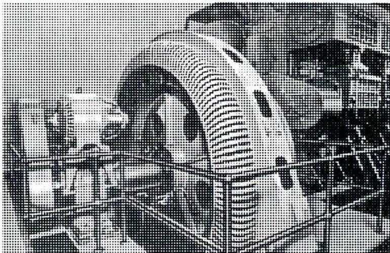 A black and white photograph showing a DC exciter generator in the foreground, connected to the rotor of a salient pole AC generator. The exciter is a smaller, cylindrical machine with visible windings and brushes, mounted on the same shaft as the larger AC generator.