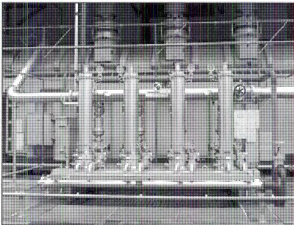 A black and white photograph of an industrial oil cooler skid. The skid is a metal frame containing several large, rectangular heat exchanger units arranged side-by-side. Various pipes, valves, and fittings are visible, connecting the units and the frame. The entire assembly is mounted on a flat, solid base.