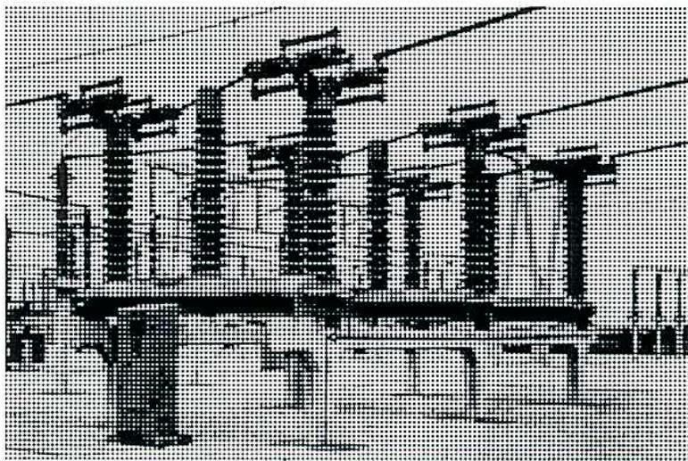 A black and white photograph showing three large, vertically-oriented airblast circuit breakers. Each unit consists of a series of horizontal insulator discs stacked on top of a central mechanical assembly. The breakers are mounted on a common base structure. The image is a halftone print with a visible dot pattern.